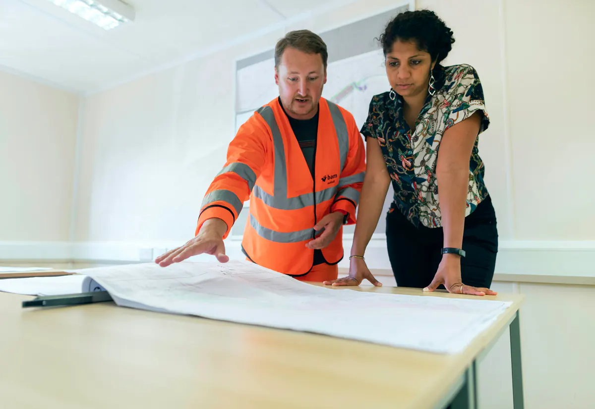 Deux ingénieurs étudient des plans techniques sur une grande table.